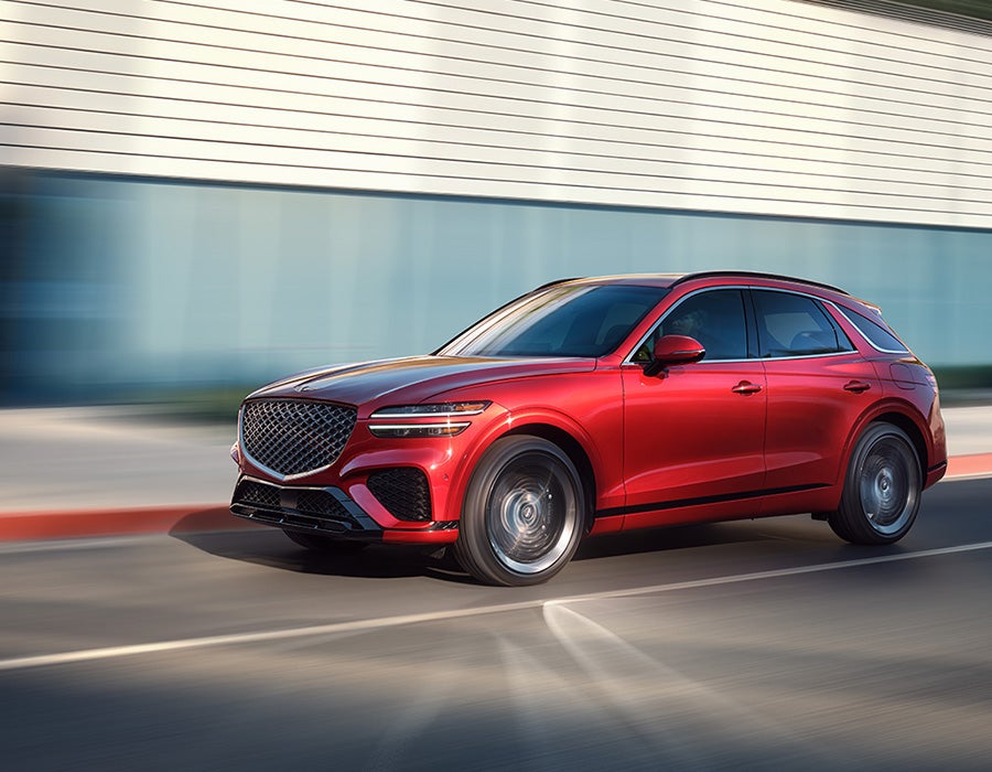 A red Genesis luxury SUV parked on a street with a blurred background, suggesting motion.