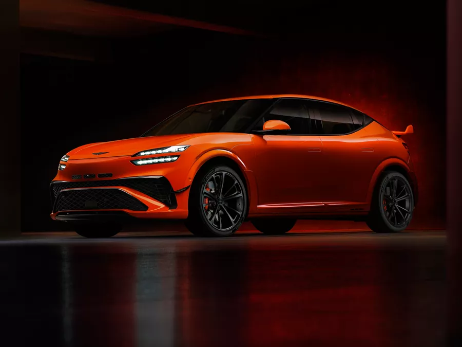 A sleek orange Genesis car with a modern design, low profile, and black accents, showcased in dramatic lighting.