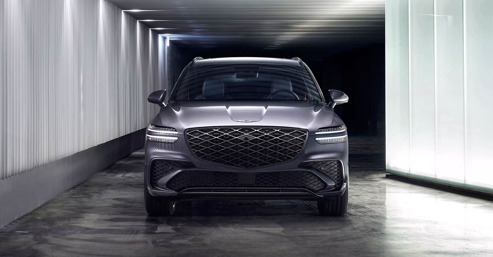 A sleek black Genesis GV70 SUV parked in a modern, illuminated indoor setting with a minimalist design.