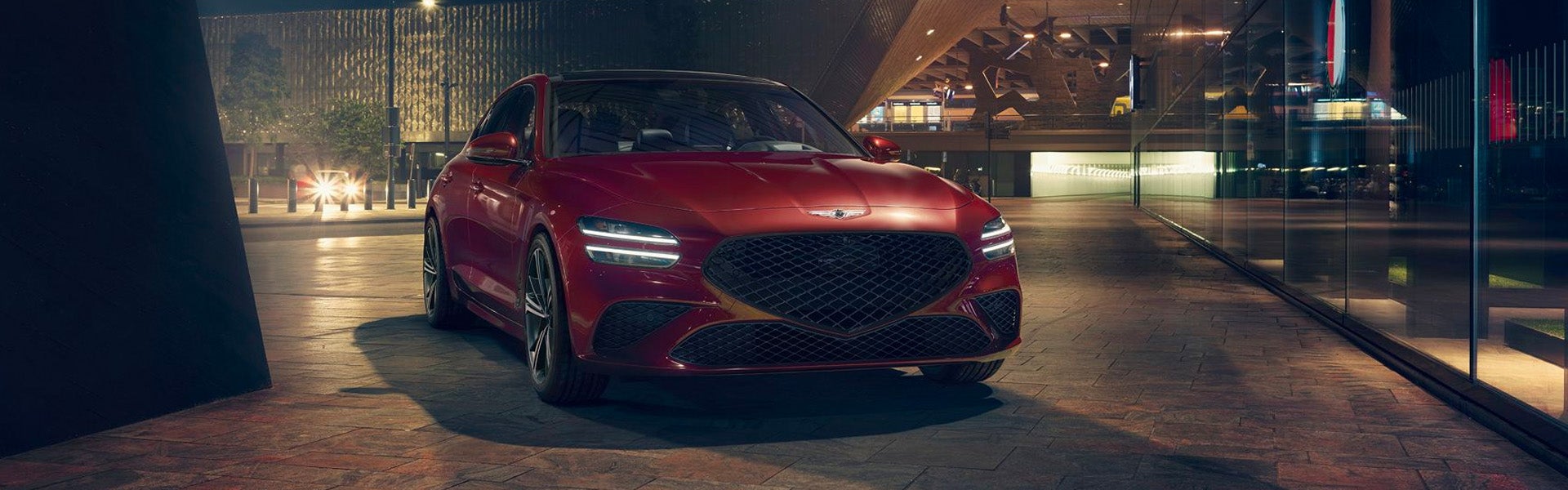 A red car parked at night in front of a modern building.