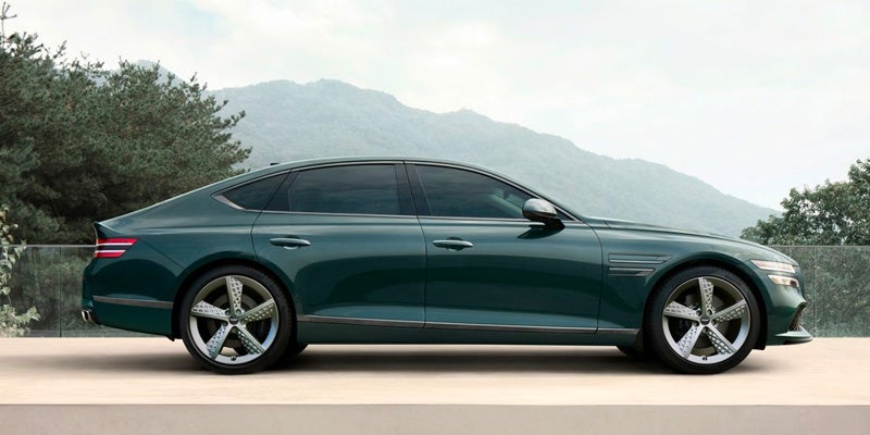 A full side profile of a dark green sedan with mountains in the background.