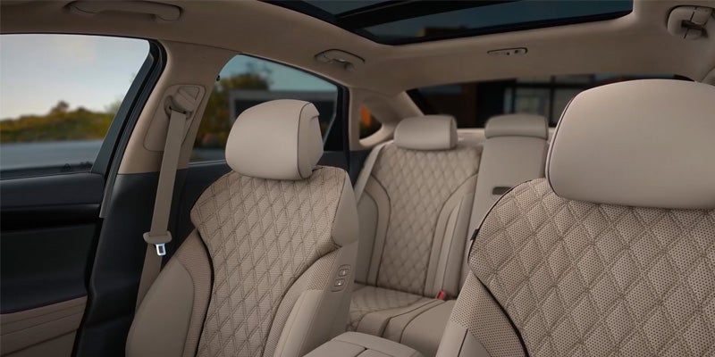 Interior of a Genesis G80 car featuring tan leather seats with a diamond quilted pattern and a panoramic sunroof.