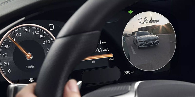 The speedometer, a digital display, and a circular display on the right showing a forward view of a silver car on the road.