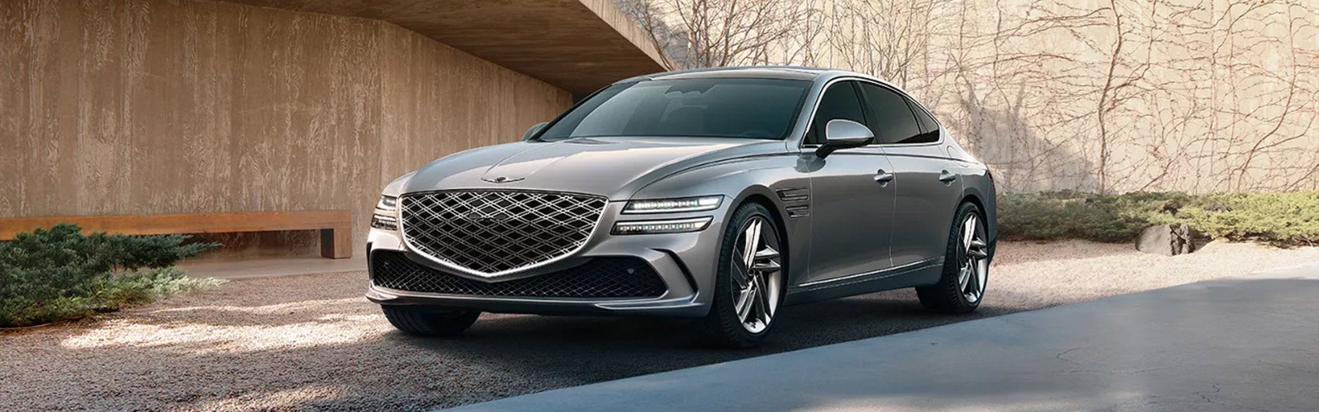 A silver Genesis G80 sedan parked outside in a modern environment.