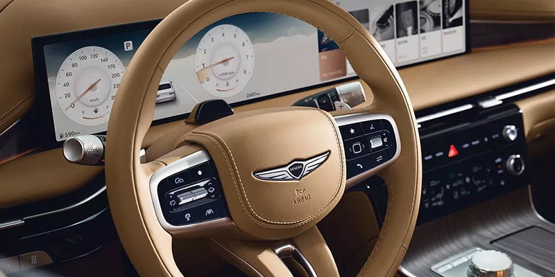 Interior view of a Genesis G80, focusing on the steering wheel, dashboard with digital displays, and elegant leather accents.