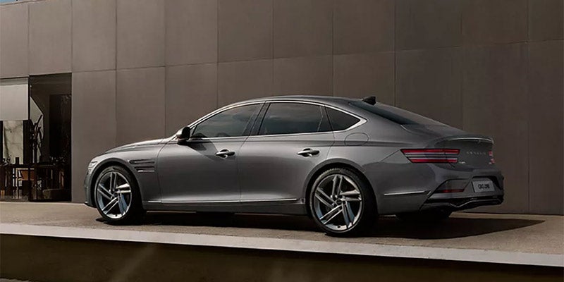 A sleek gray Genesis G80 sedan parked on a concrete platform with a modern architectural background.