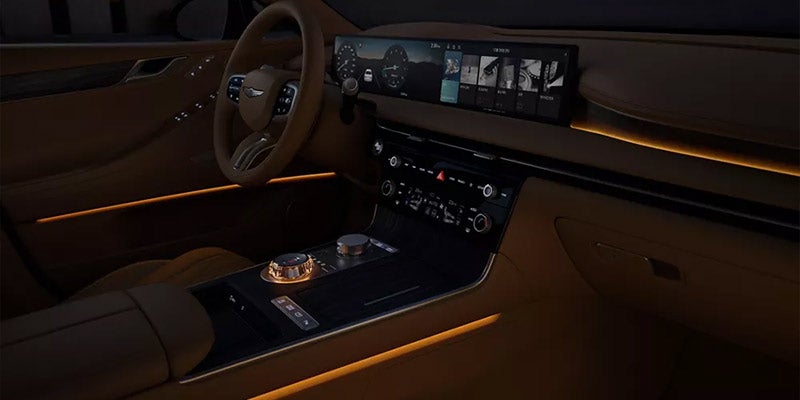 Interior view of a Genesis G80, showcasing a sleek dashboard with a large display screen, buttons, and ambient lighting highlighting the design features.