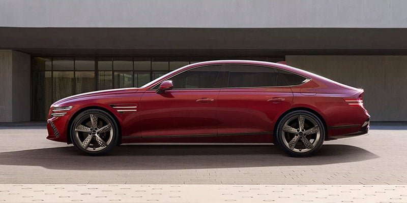 A sleek, red Genesis G80 parked in front of a modern building.