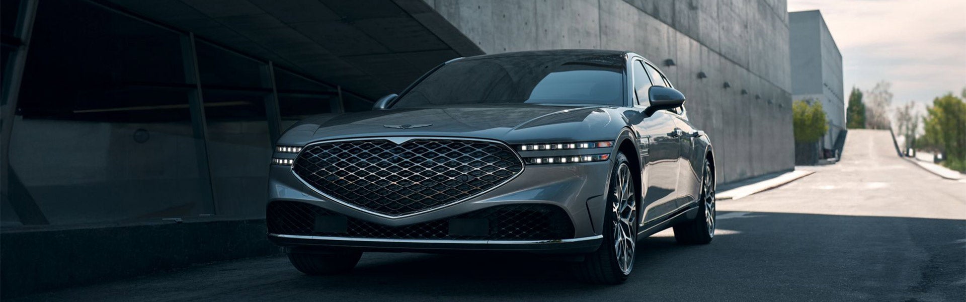 A gray car with its headlights on, parked outside a building