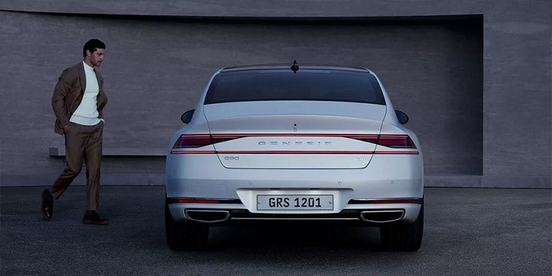 A man in a suit walking toward a white car from the rear.