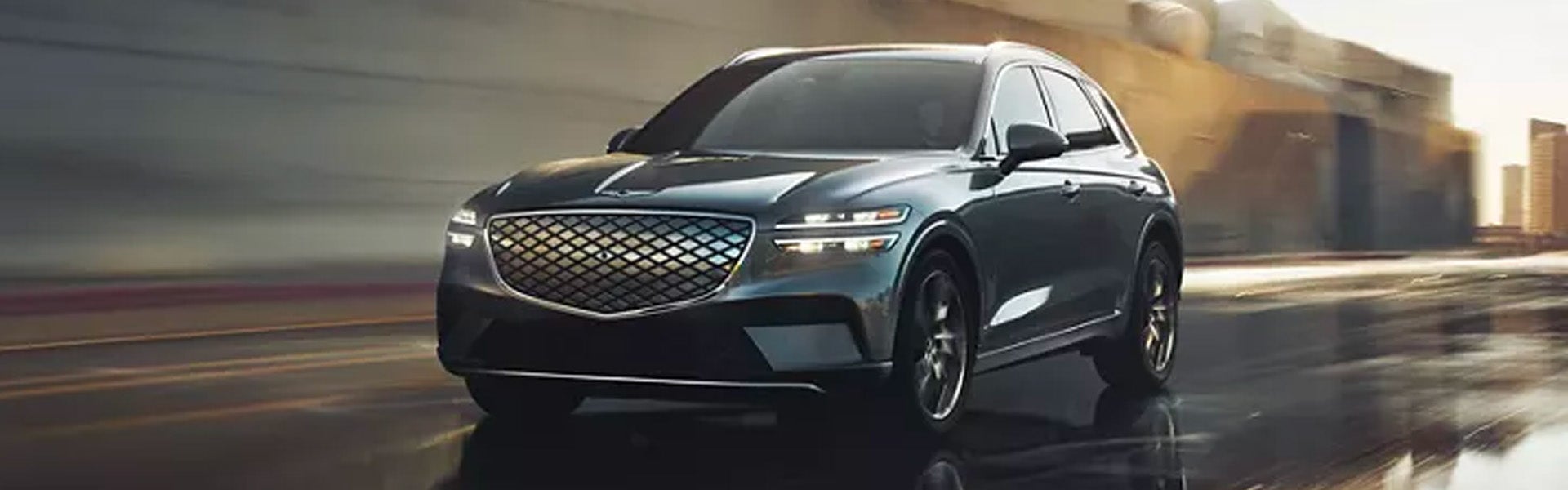 2026 Genesis GV70 luxury SUV driving through a city roadway with a sleek exterior design and signature Genesis grille.
