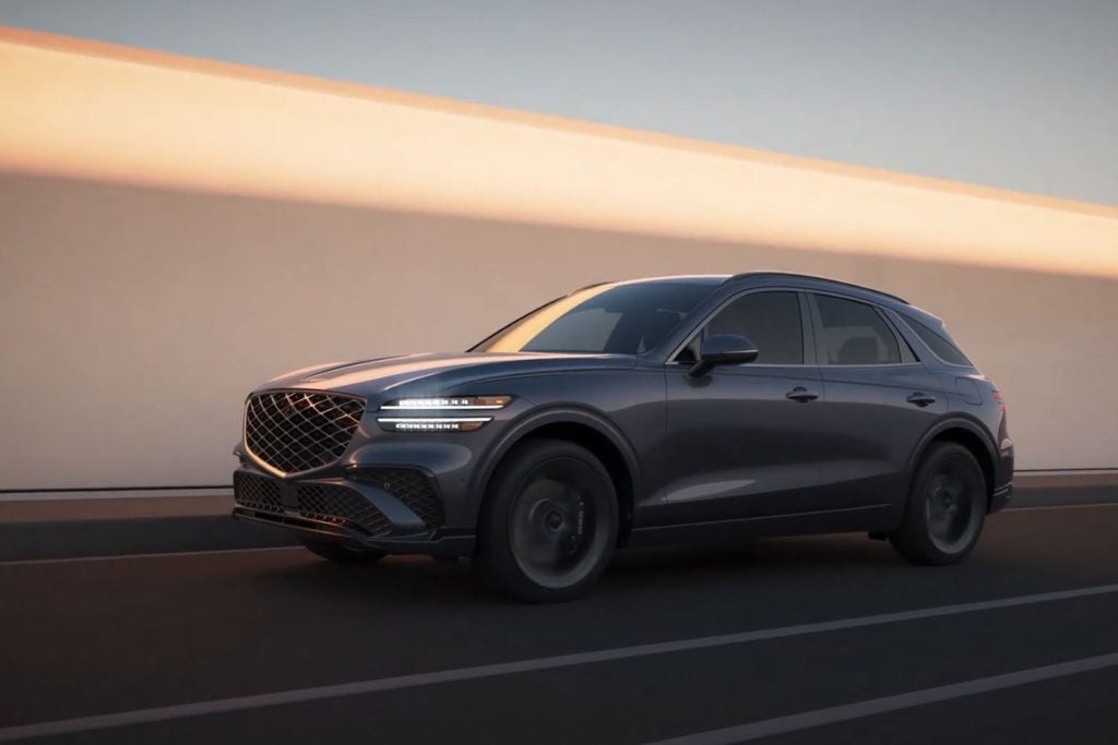 A luxury Genesis SUV driving on a modern road with a sunset backdrop.
