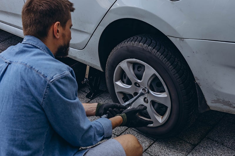 A man in gloves is using a wrench to change a tire on a car.